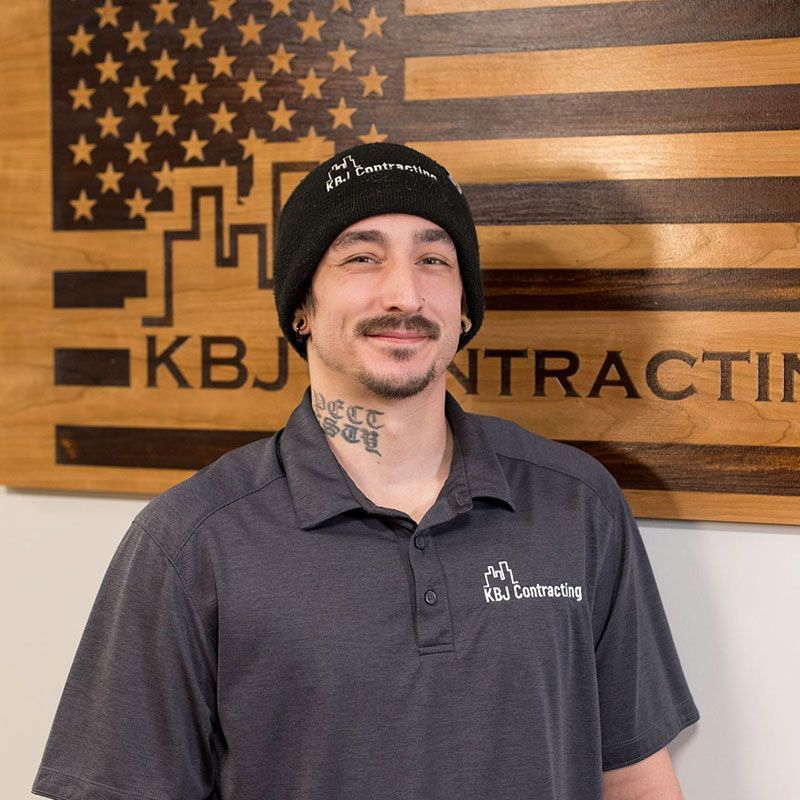 A man is standing in front of a sign that says kbj contracting