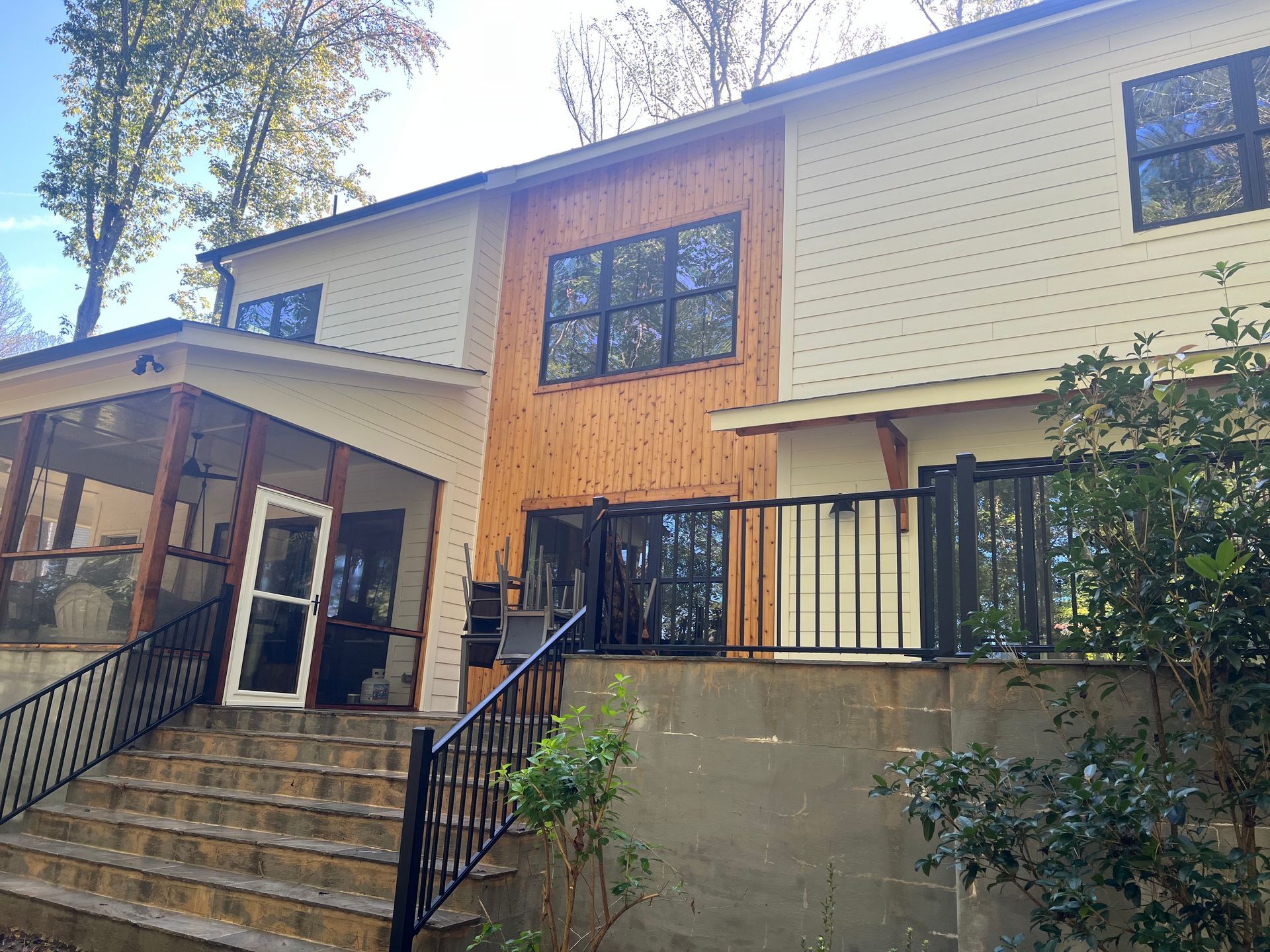 Two-story house with a wood-paneled accent and a screened porch. Black railing leads to a deck.
