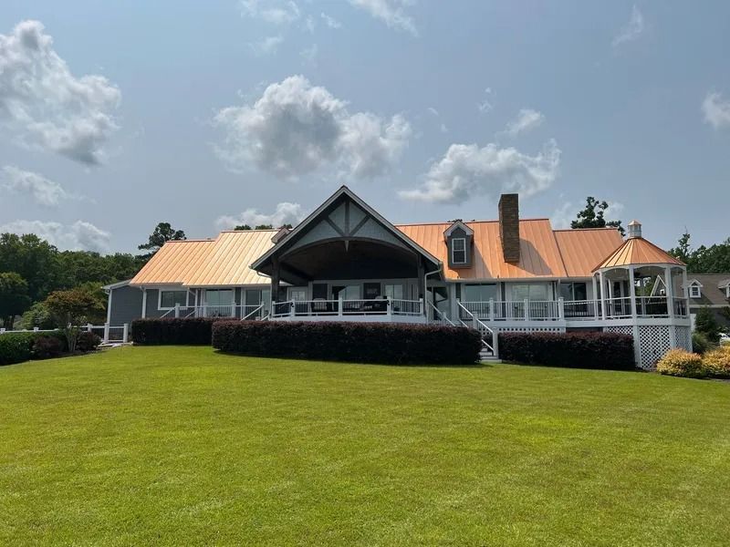 House with copper roof, porch, and green lawn against a cloudy sky.
