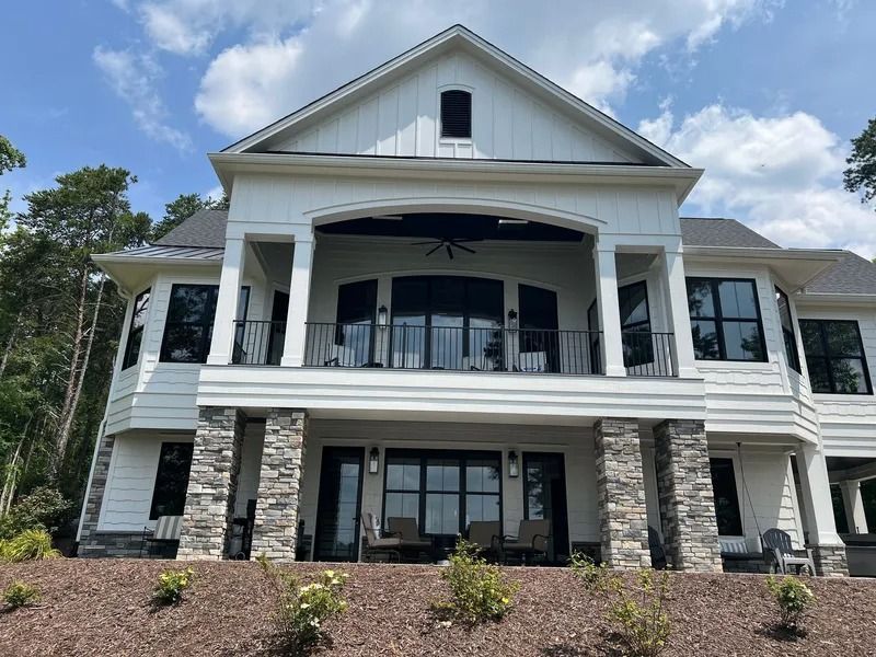 White house with black windows, stone columns, and an upper-level balcony under a blue sky.