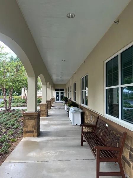 Covered walkway with beige walls, brown bench, and large windows.
