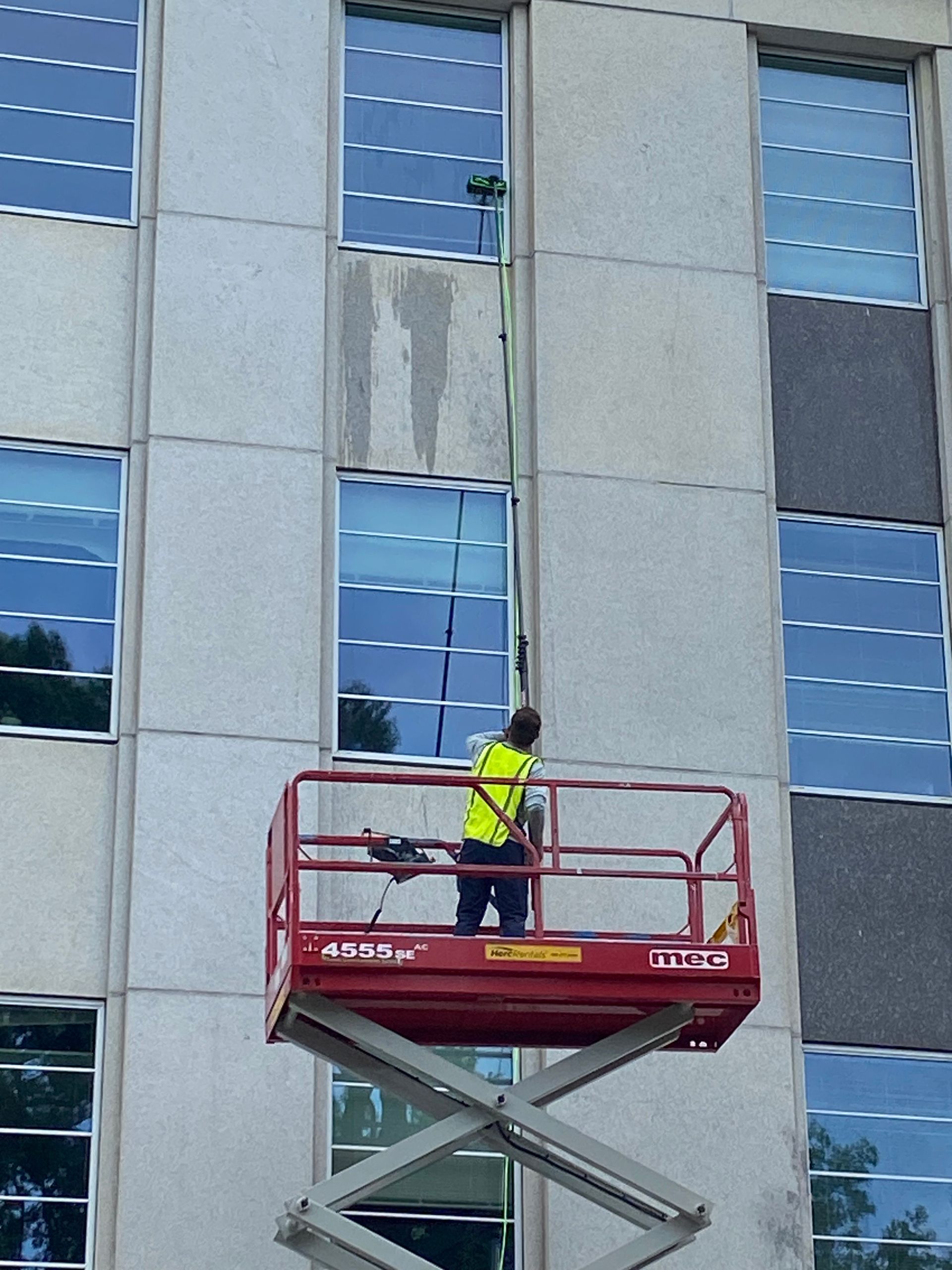 A worker on a red lift cleans windows on a gray building.