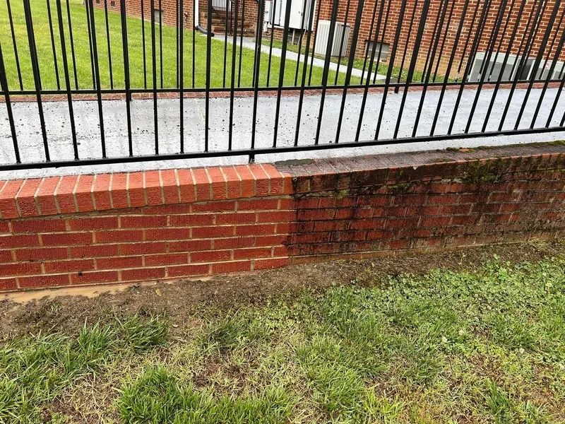 Brick wall, half cleaned, shows contrast; black railing above, grass below.