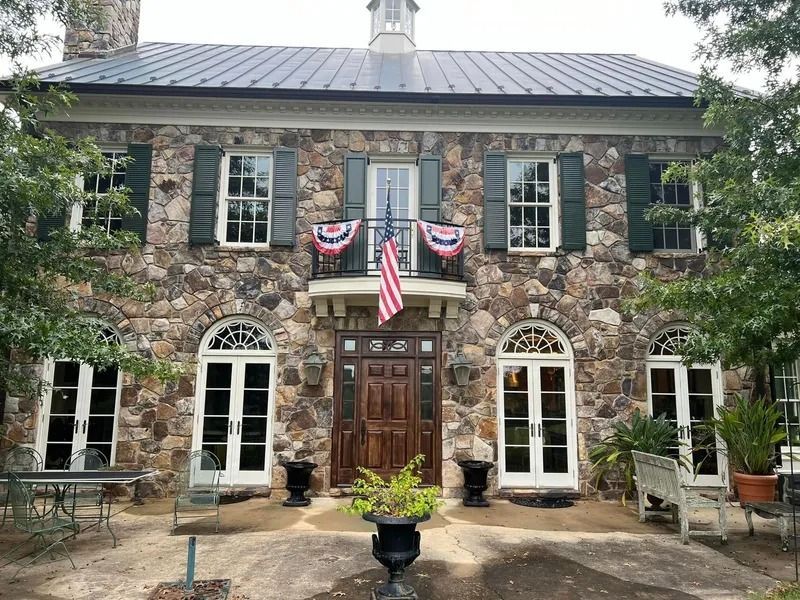 Stone house with American flag, green shutters, white-framed windows, and a balcony.