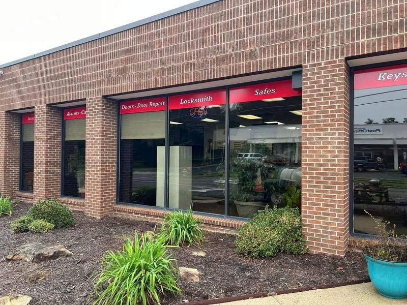 Brick building storefront: Jackson & Son's door repair, locks, and safes. Red signs above windows. Green bushes in front.