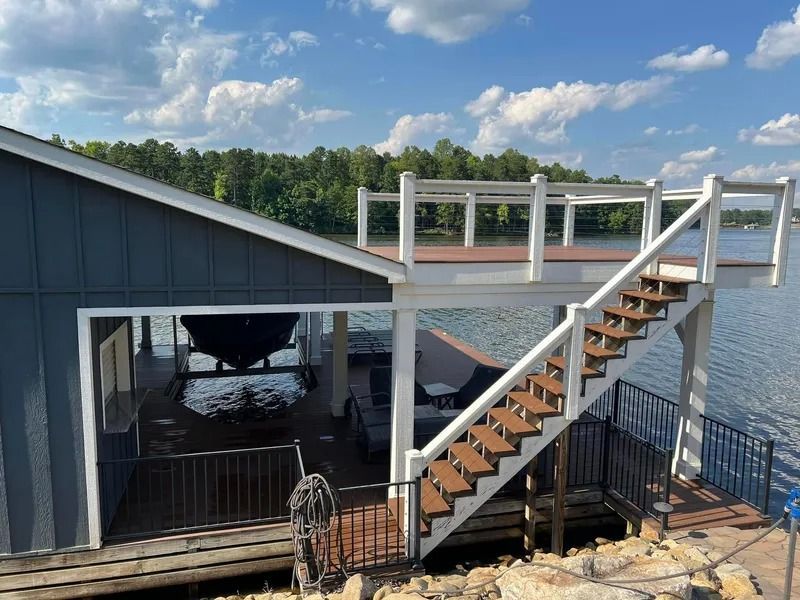 Boathouse with stairs leading to a deck overlooking a lake. Blue house, white railings, brown stairs.