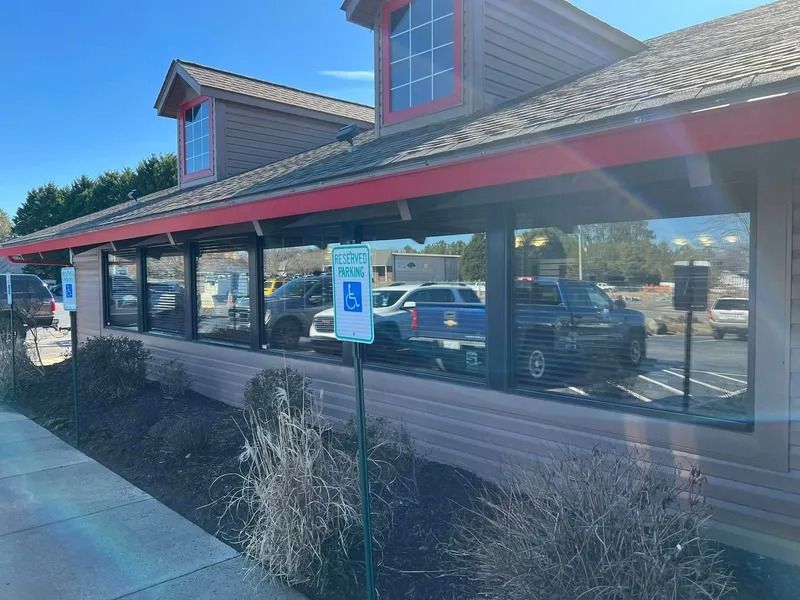 Exterior view of a restaurant with large windows, a red roof, and a handicap parking sign.
