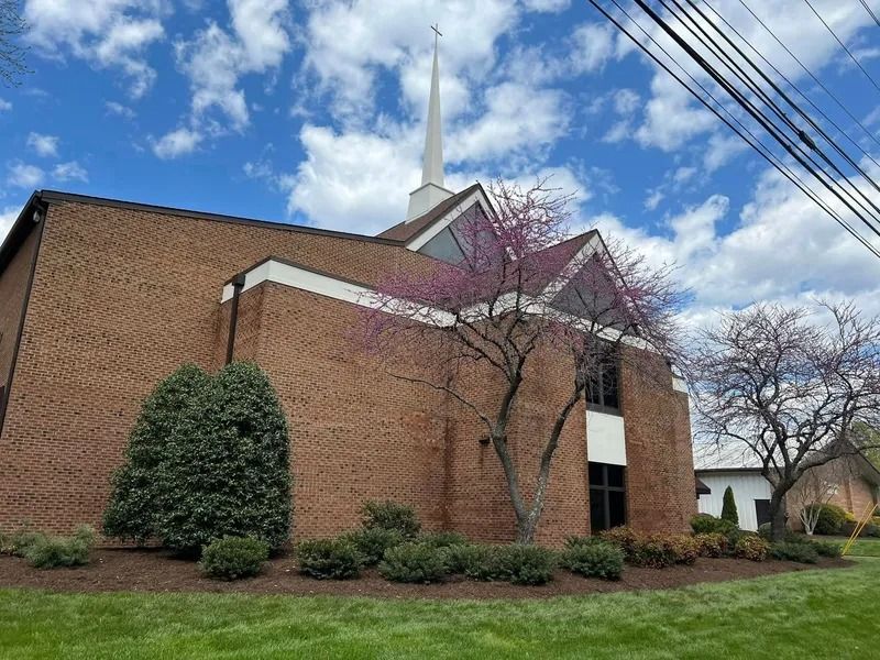 Brick church with white steeple and blooming tree under a blue sky.