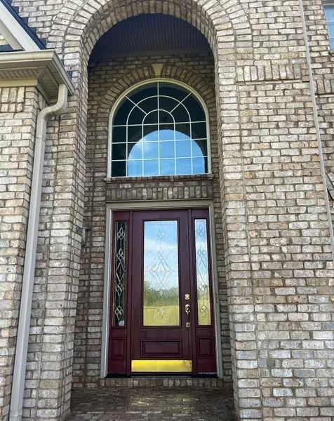 Brick facade with arched window above a burgundy door.