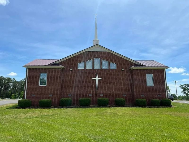 Brick church with a cross on the front, green lawn, blue sky.