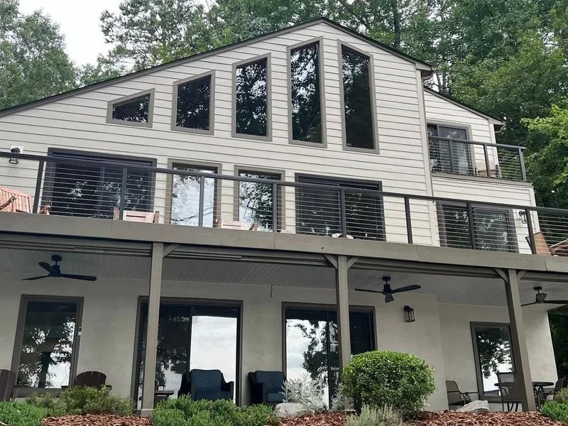 Two-story house with a large deck. Windows and doors, grey siding, with trees in the background.
