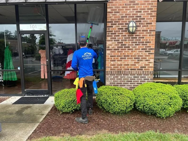A person in blue shirt cleans the windows of a storefront.