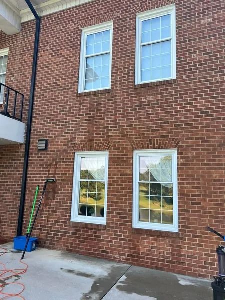 Brick building with four white-framed windows. Black downspout runs beside it. Equipment below.