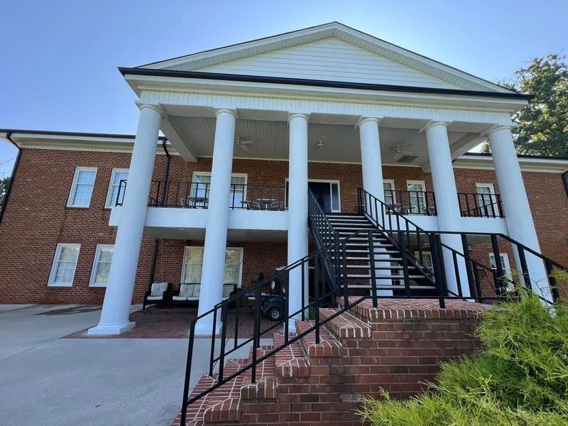 Brick building with white columns and black staircase leading to a second-story porch.
