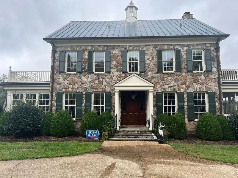 Stone house with green shutters, white trim, and a gray roof.