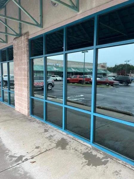 Storefront with blue-framed windows reflecting a parking lot and cars; exterior shot.