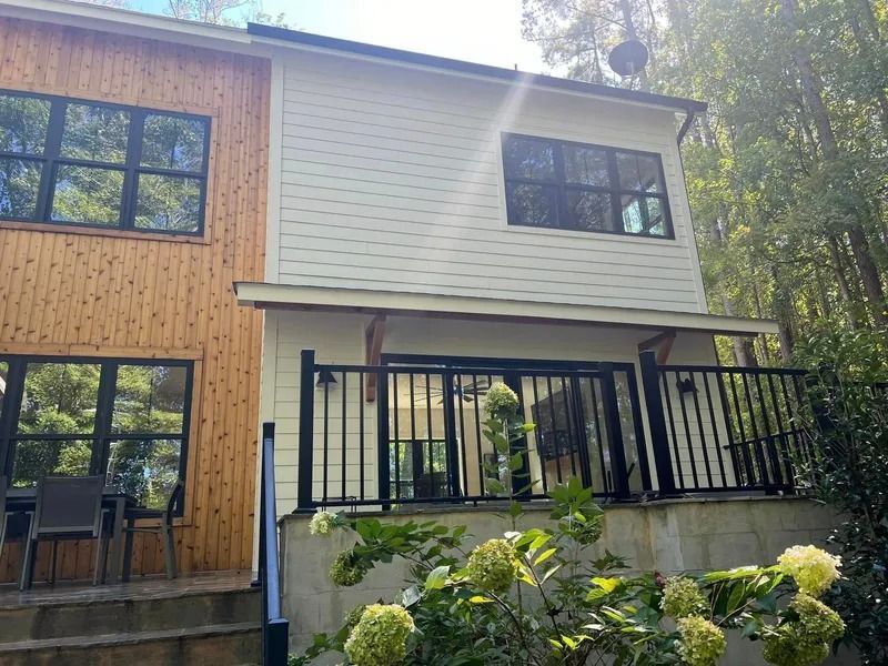 Two-story house with white siding and a brown wooden side, black windows, and a deck.