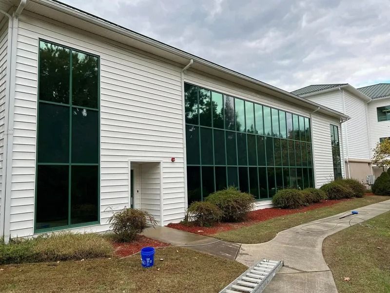 White building with tinted windows, shrubs, and a sidewalk on a cloudy day.
