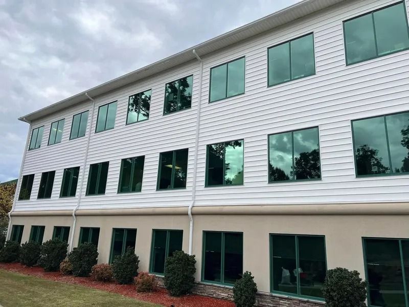 Two-story building with white siding, green-tinted windows, and landscaping. Overcast sky.