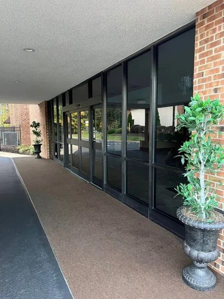 Entrance with tinted windows and automatic doors, flanked by brick and potted plants.