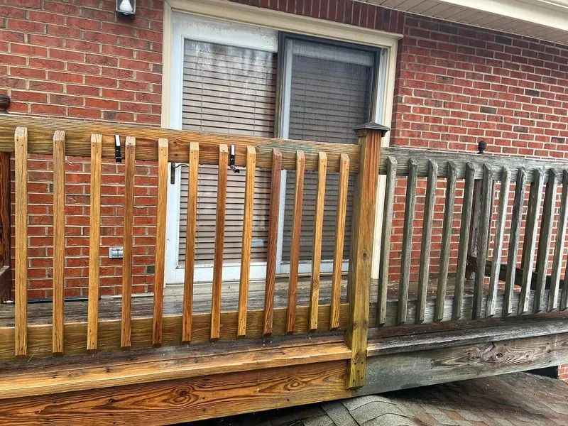 Wooden deck railing, half cleaned showing bright wood, against a brick wall with sliding glass door.