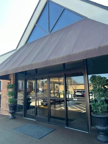 Entrance with brown awning, glass doors, and two potted topiary trees.