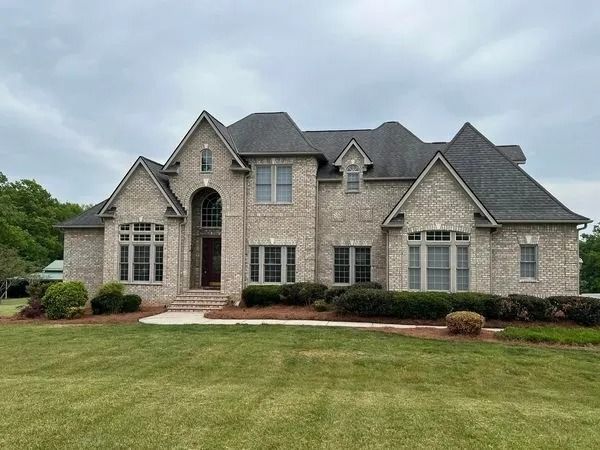 Two-story brick house with dark roof, arched entryway, and manicured lawn on a cloudy day.