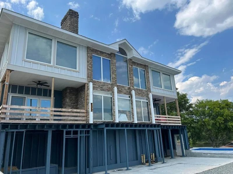 Two-story house with stone accents, large windows, and a blue foundation against a blue sky.
