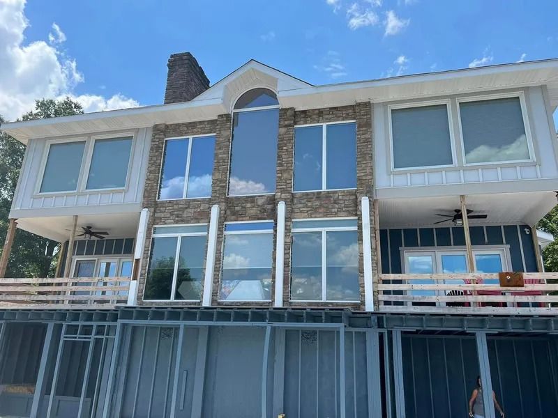 Two-story lake house with stone facade and large windows, under construction.