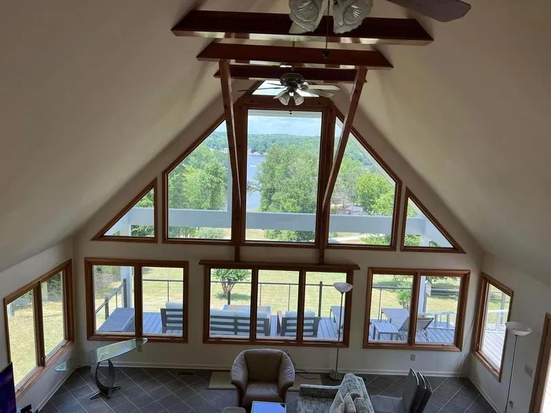 Interior view of a high-ceilinged room with large windows, a deck, and outdoor view of a lake.