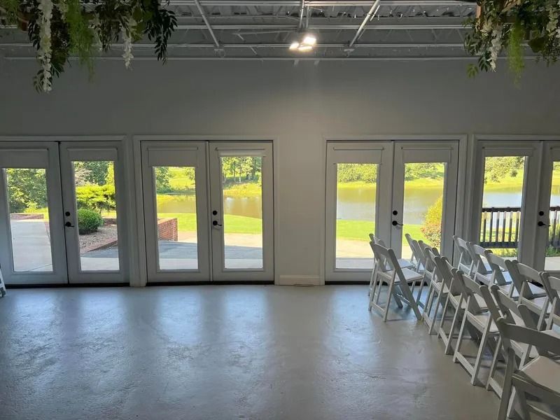 White room with glass doors overlooking a lake, lined with white chairs.