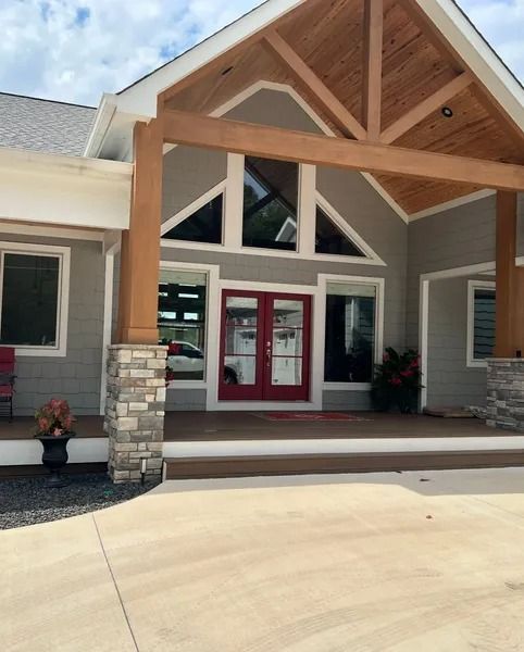 Gray building with red doors, wooden beams, stone accents, and a concrete driveway.