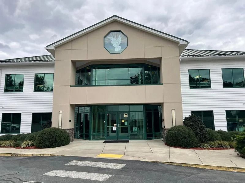 Two-story beige building with glass doors and windows, bushes, and a crosswalk on the sidewalk.