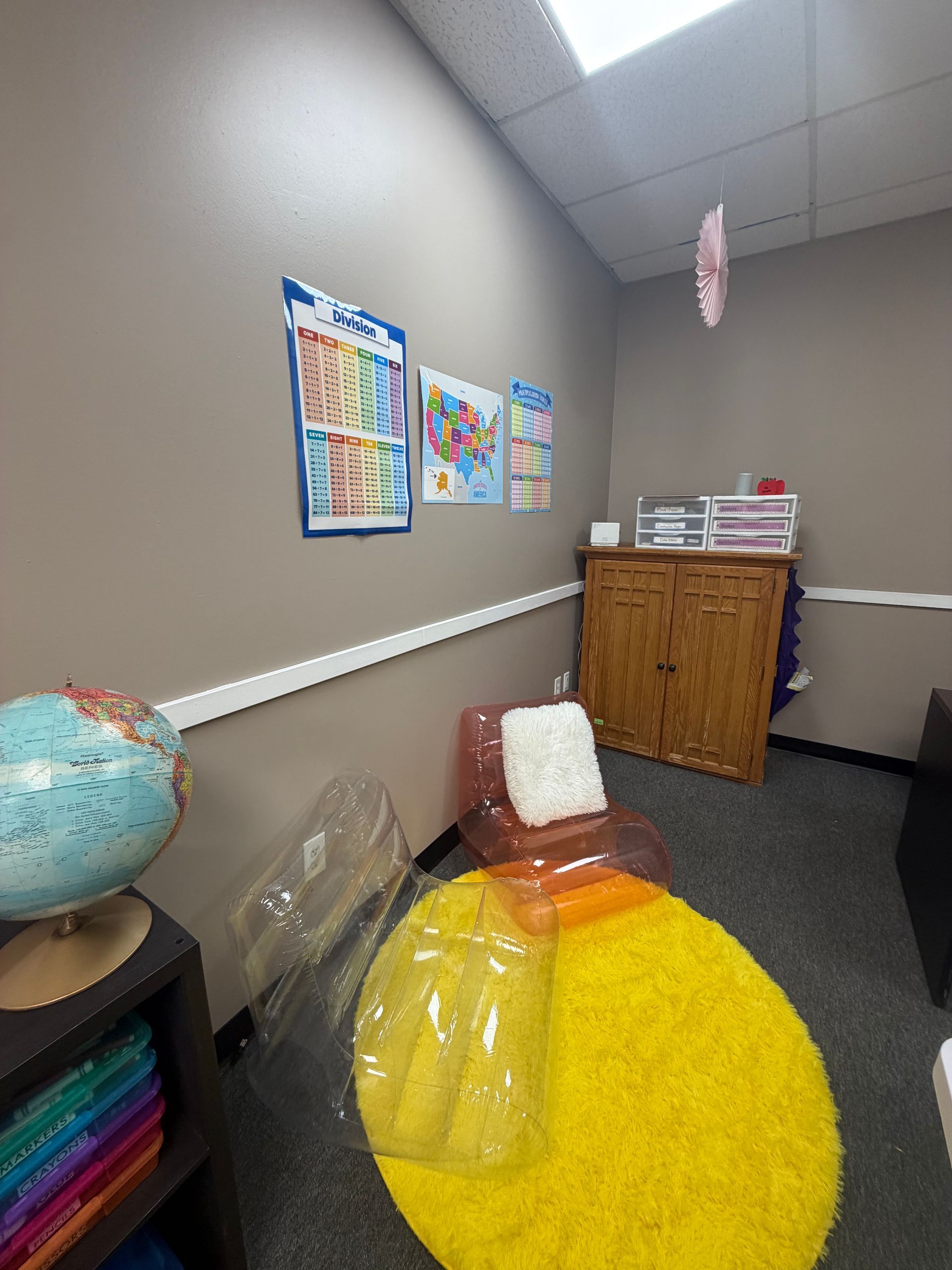 Small classroom corner with colorful wall charts, globe, cabinet, and a bright yellow bean bag chair.