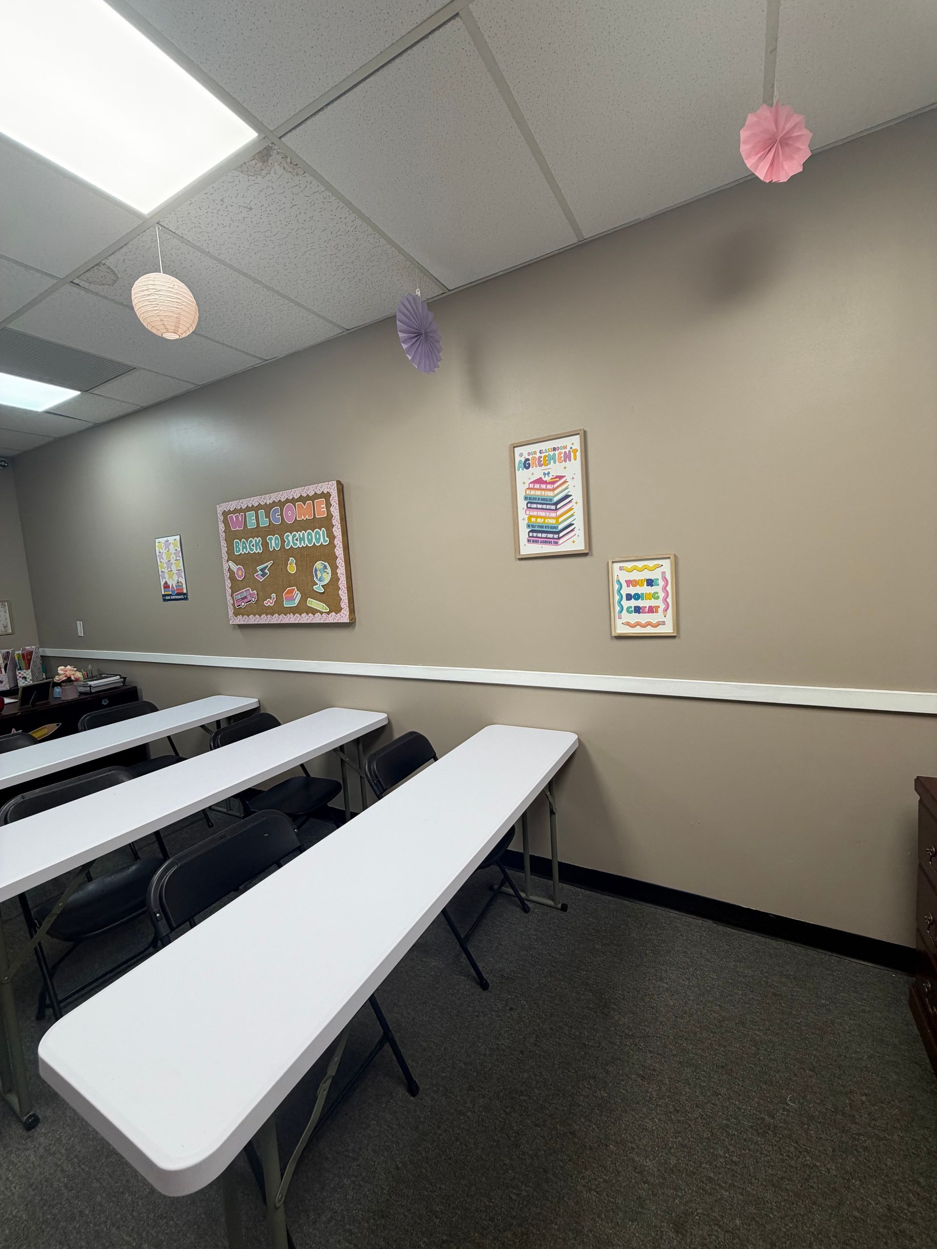 Classroom with white desks, bulletin boards, and pastel paper lanterns hanging from the ceiling