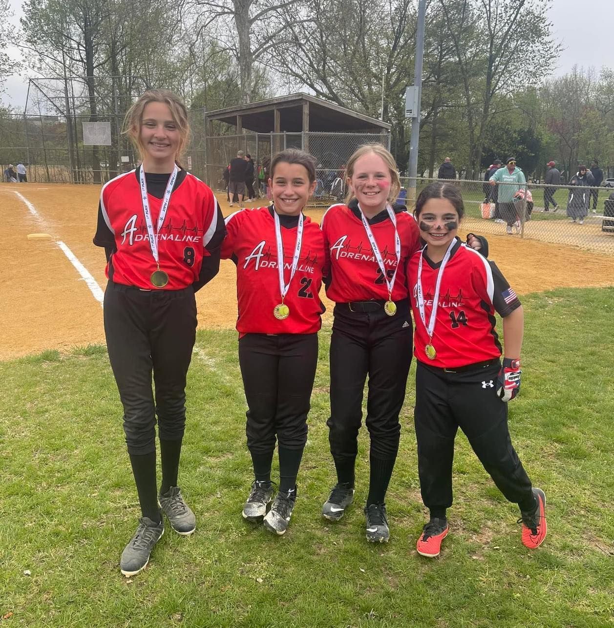 Four medal-winning runners in red jerseys posing on a grassy field at a track meet