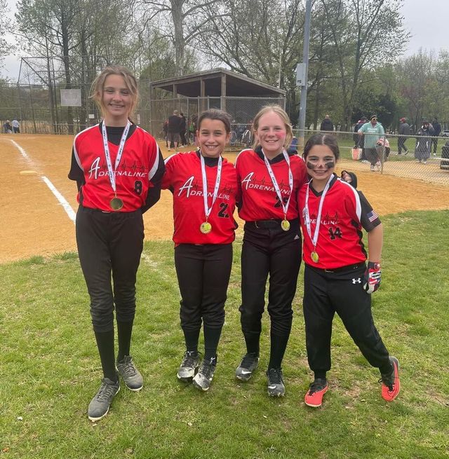Four athletes in red jerseys with medals stand on a grassy field after a race