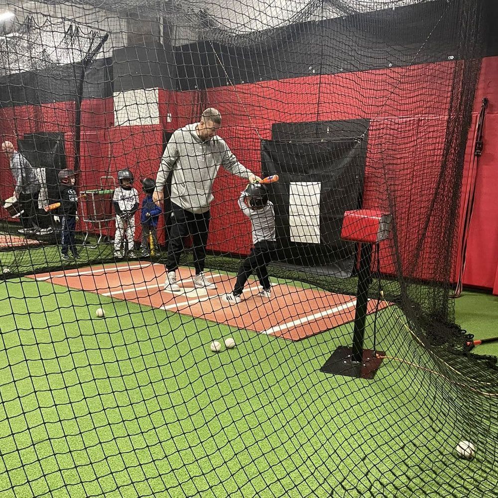 Indoor baseball batting cage with a coach and child practicing hitting off a tee.