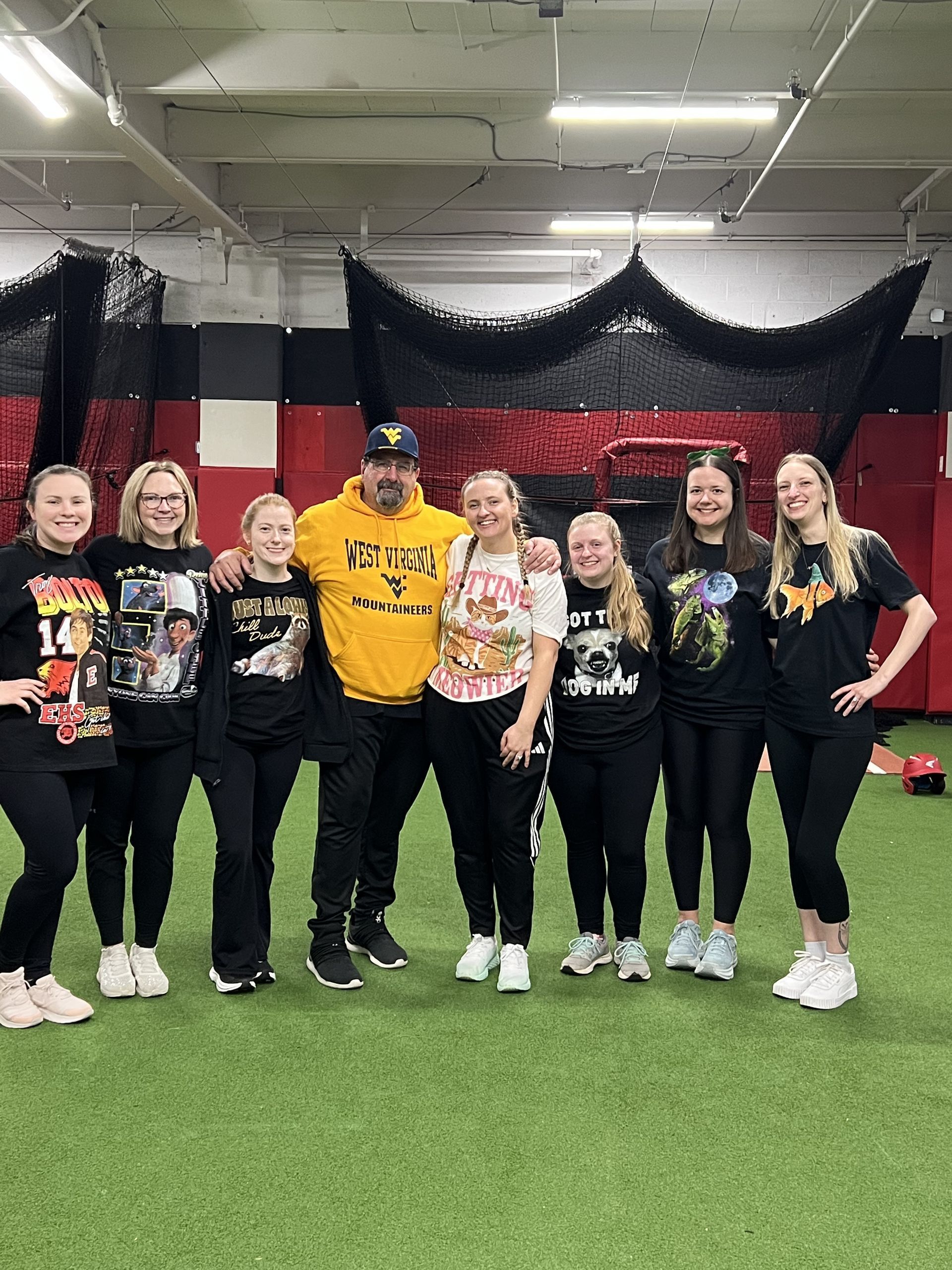 Group of nine people posing indoors on turf, wearing matching black and yellow shirts with a draped black-red-white backdrop.