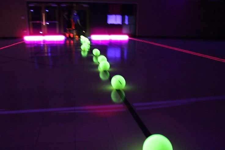 Glowing green balls lined up on a dark indoor floor, lit by pink neon lights in the distance