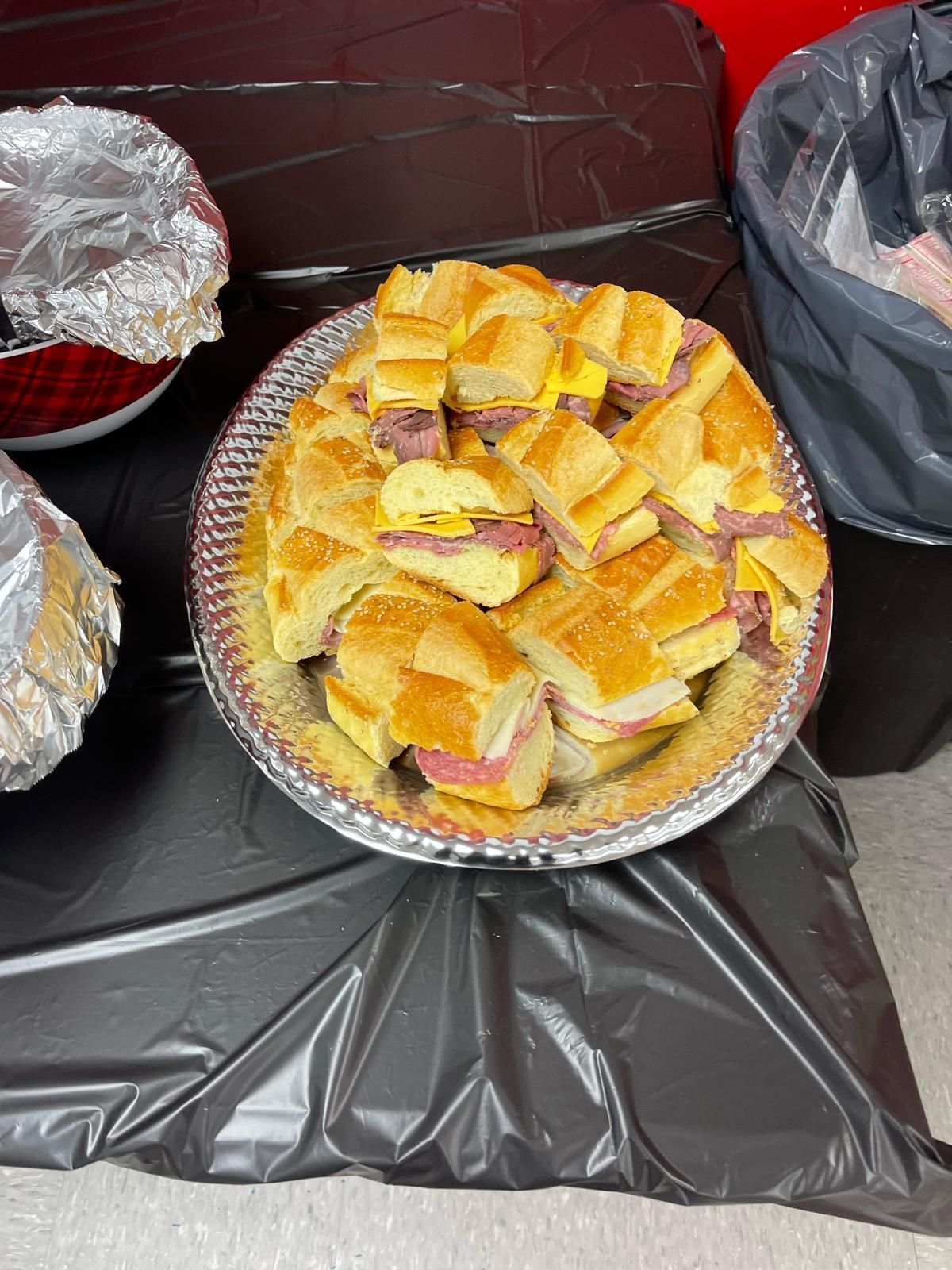 Tray of small square sandwiches on a black tablecloth, with foil-wrapped food trays nearby.