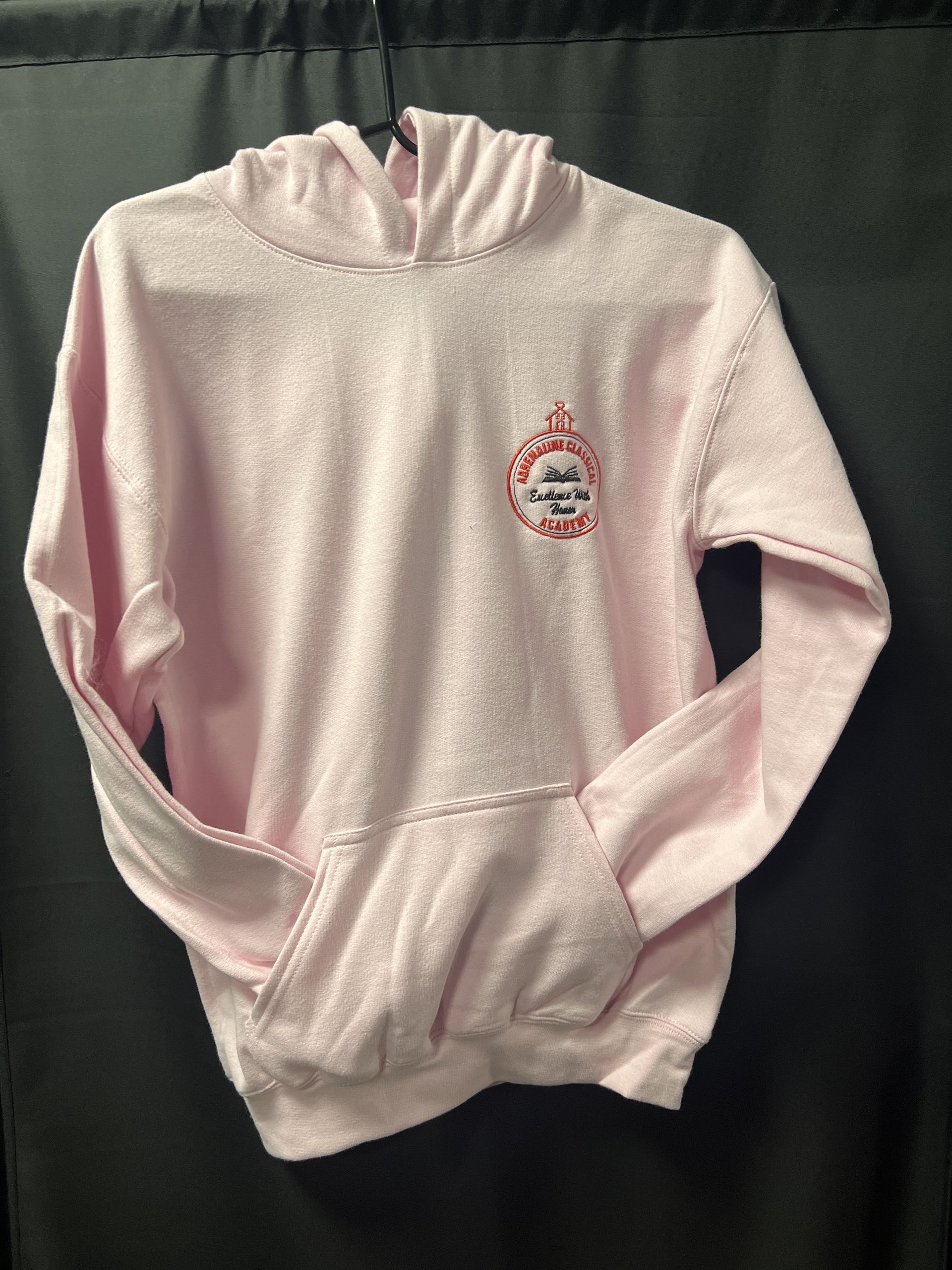Light pink hooded sweatshirt with a small chest logo, laid flat against a dark background.