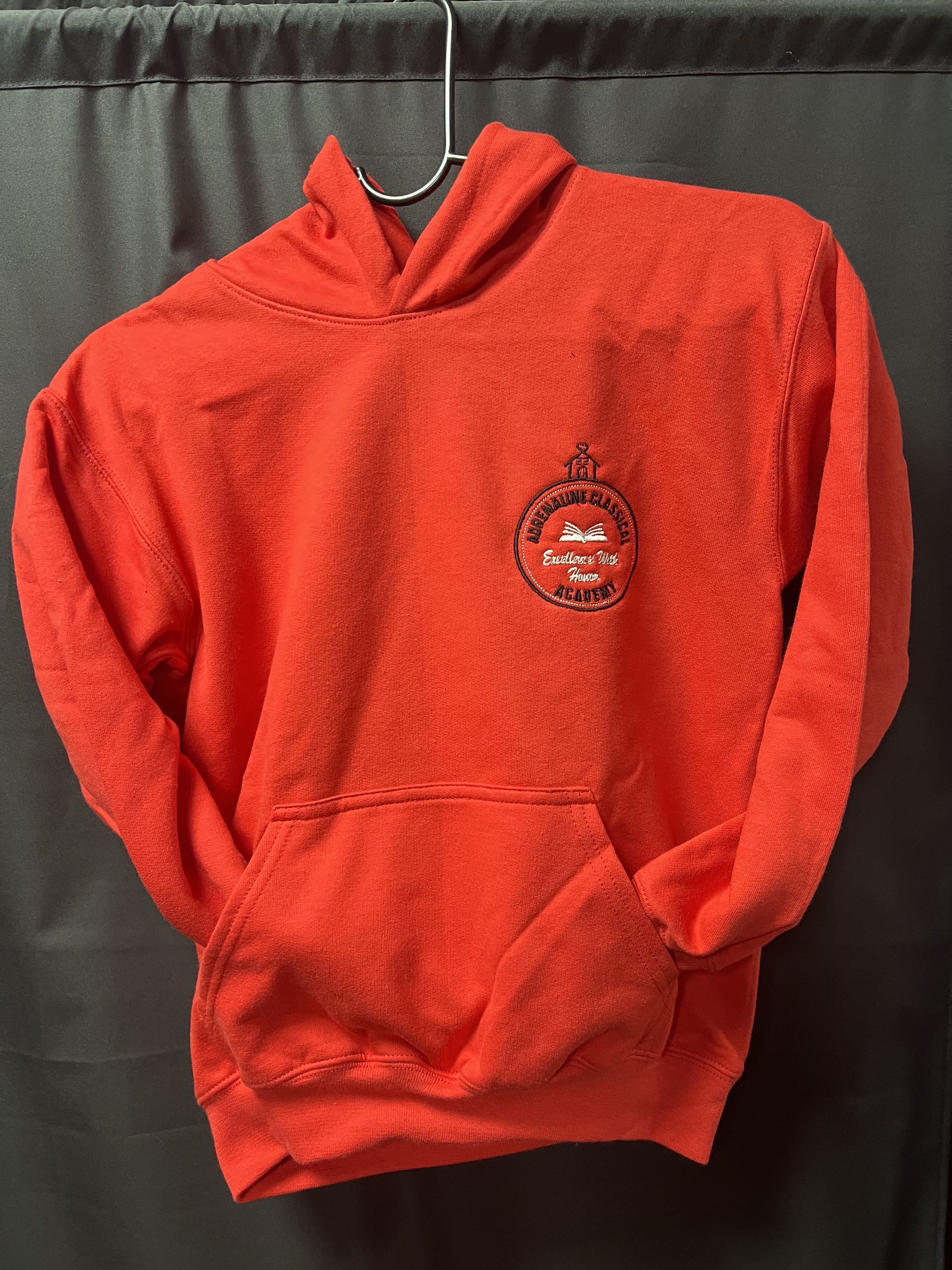 Red hooded sweatshirt hanging against a dark curtain, with a small chest logo.