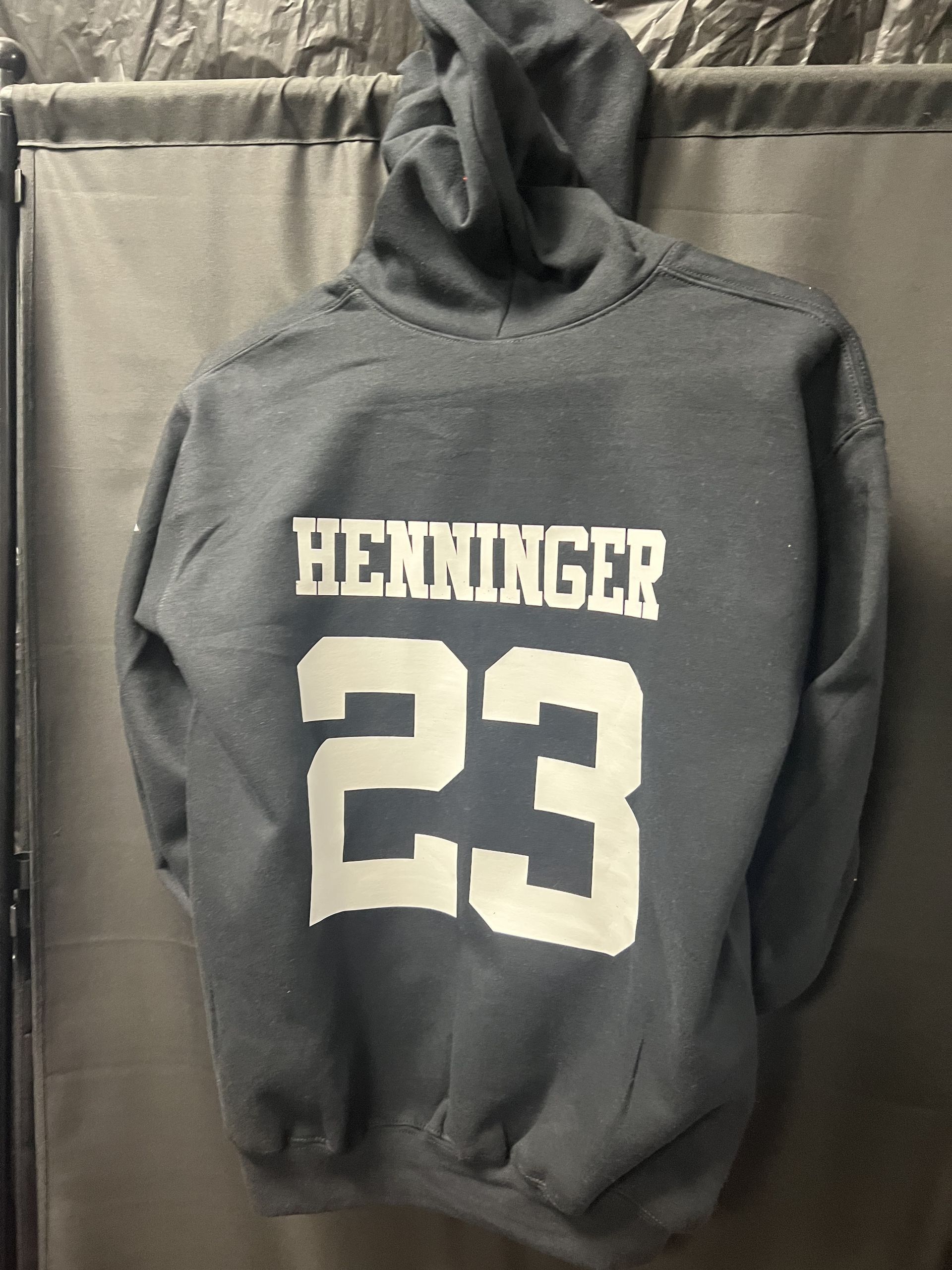 Black hoodie with “HEDDINGER” and large white number 23 hanging against a gray backdrop