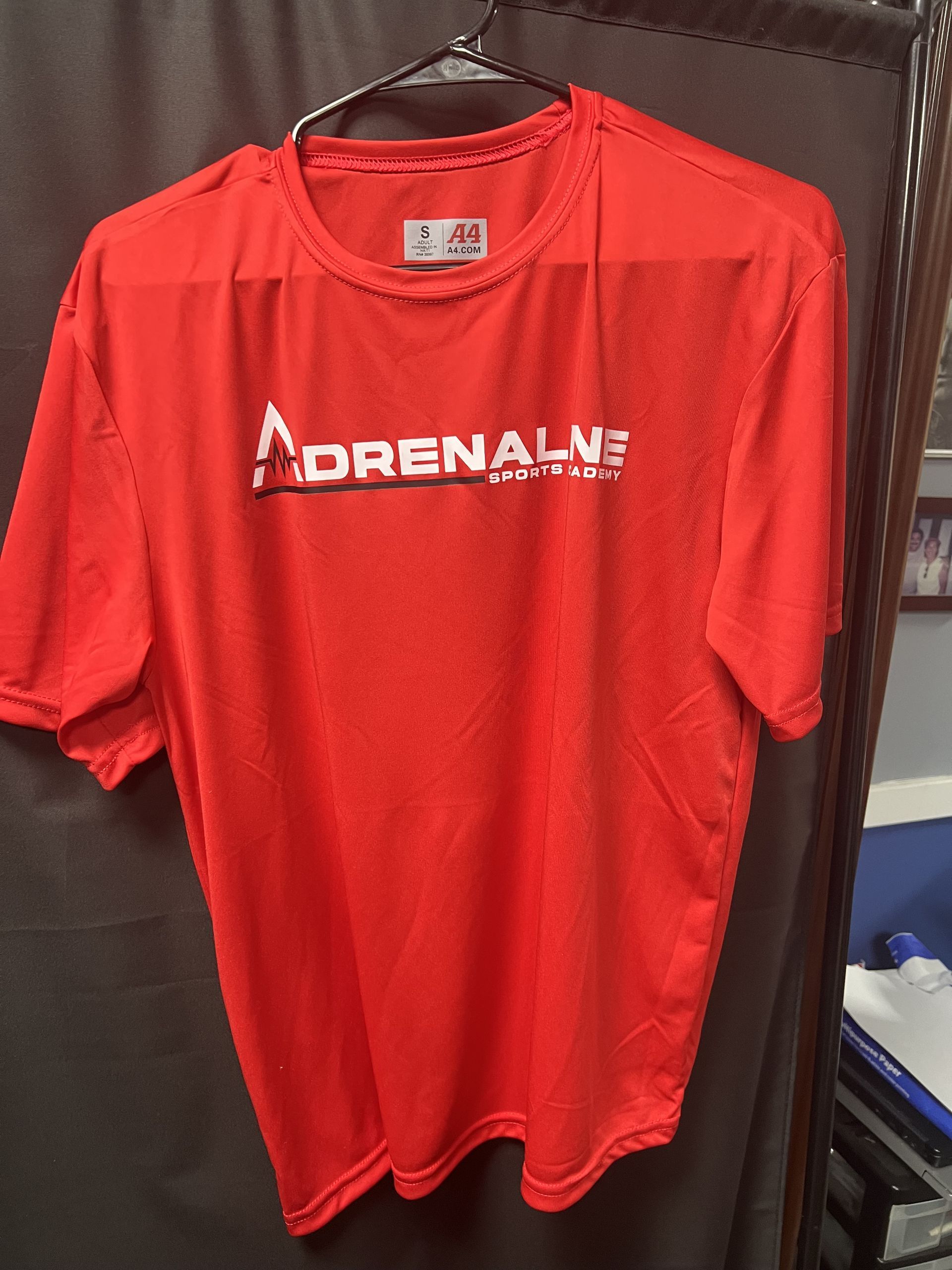Red Adidas-style T-shirt hanging on a hanger against a dark background