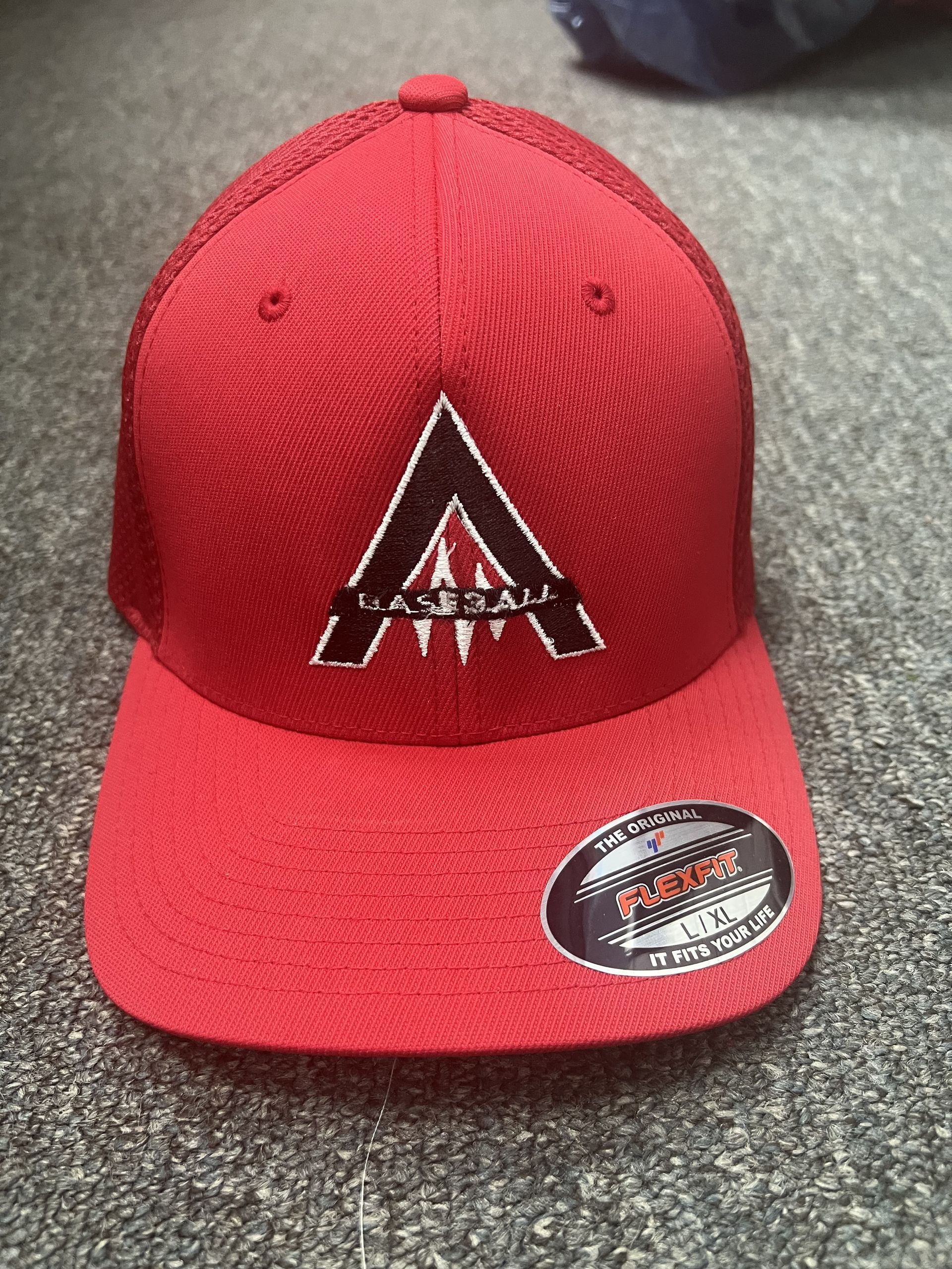 Red baseball cap with a black-and-white triangular logo on the front, shown on a countertop.