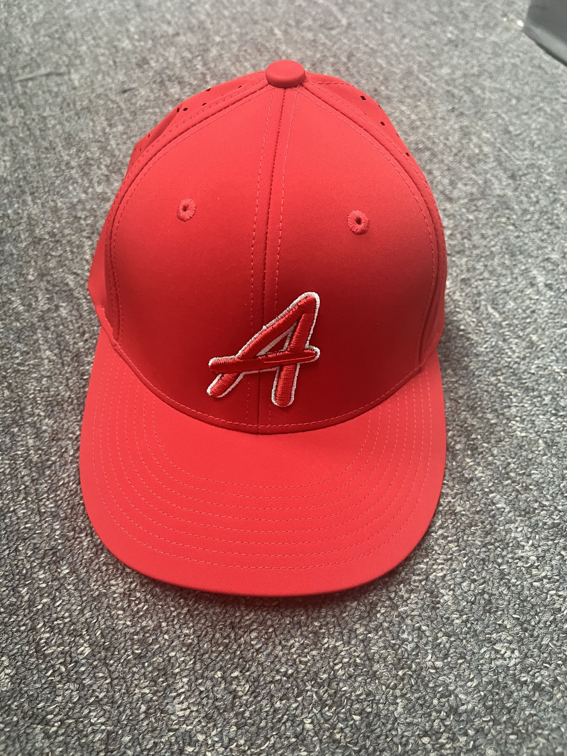 Red baseball cap with a stitched lowercase “a” logo on a gray surface