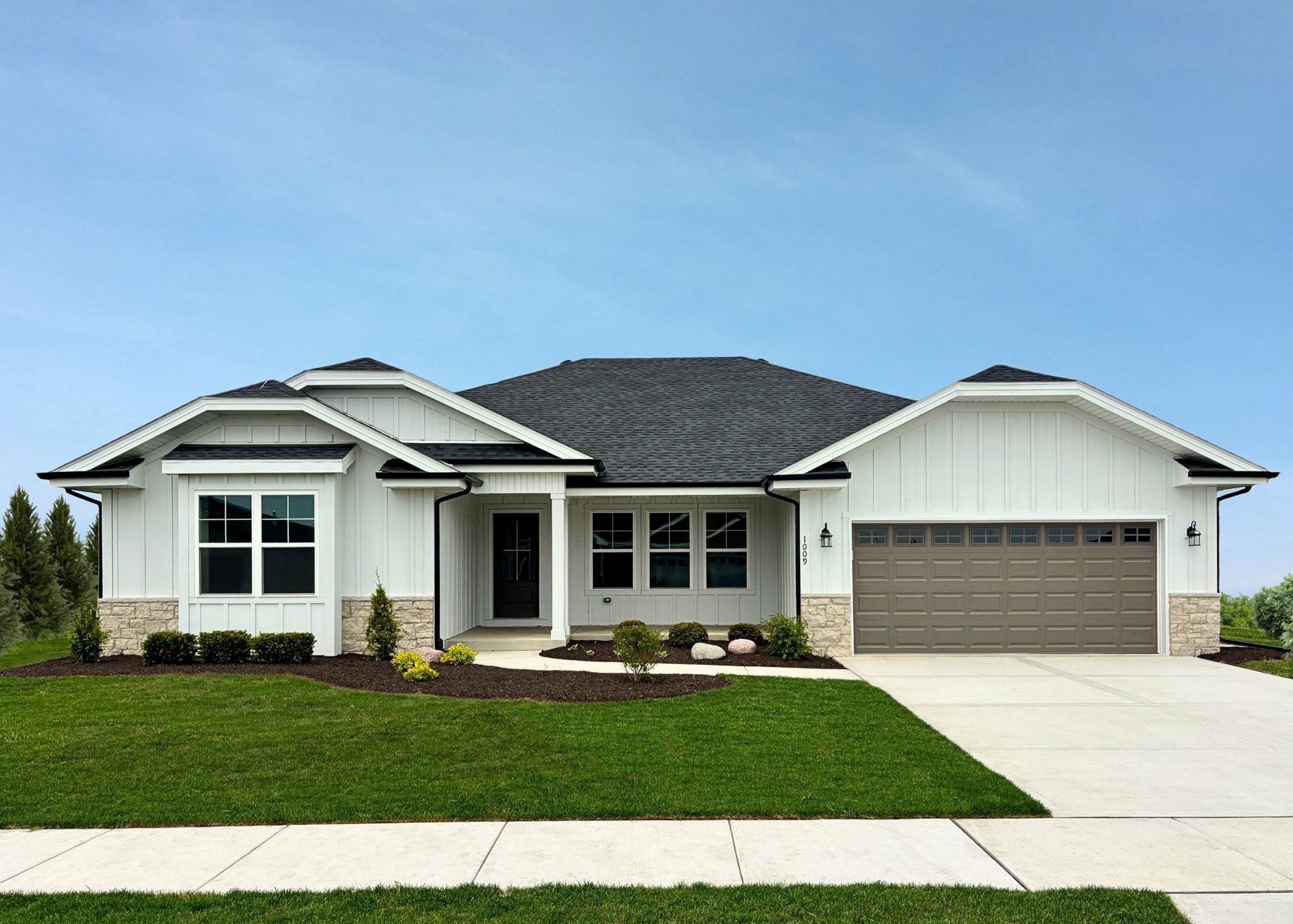 A white house with a gray garage door is sitting on top of a lush green lawn.
