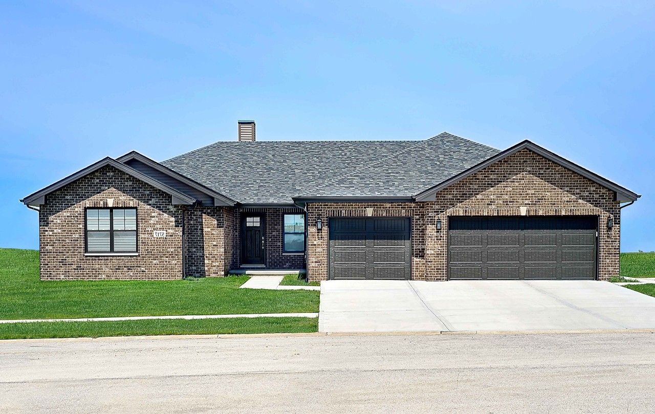 A brick house with a gray roof and black garage doors.