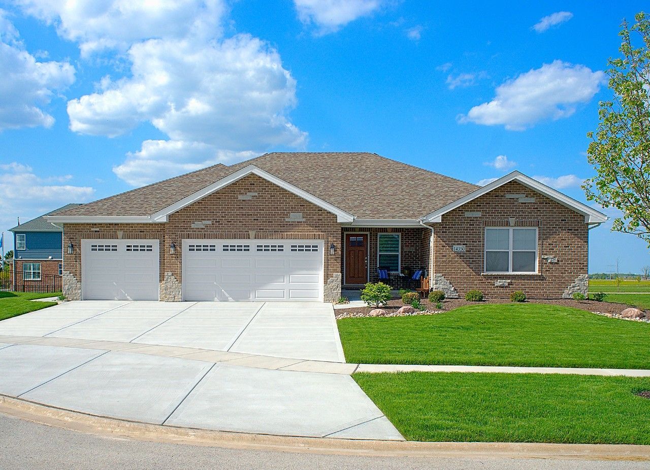 A brick house with two garage doors and a concrete driveway.